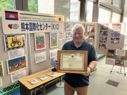 シャムリアップ州からの感謝状を持ちパネルの前に立つ谷川理事長