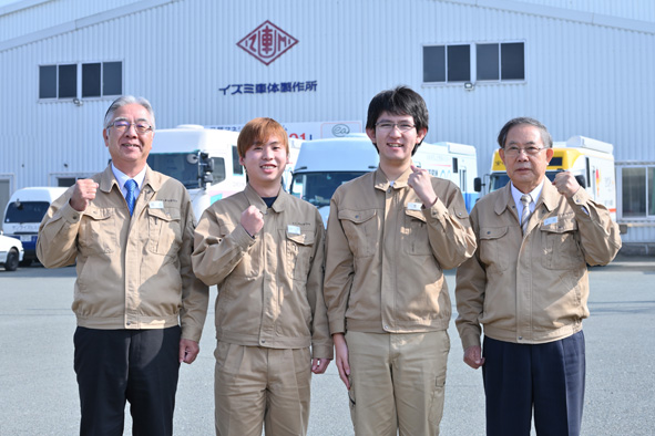 大津町にある本社工場をバックに新入社員と一緒に。左端が國武幸弘社長、右端が古庄忠信会長